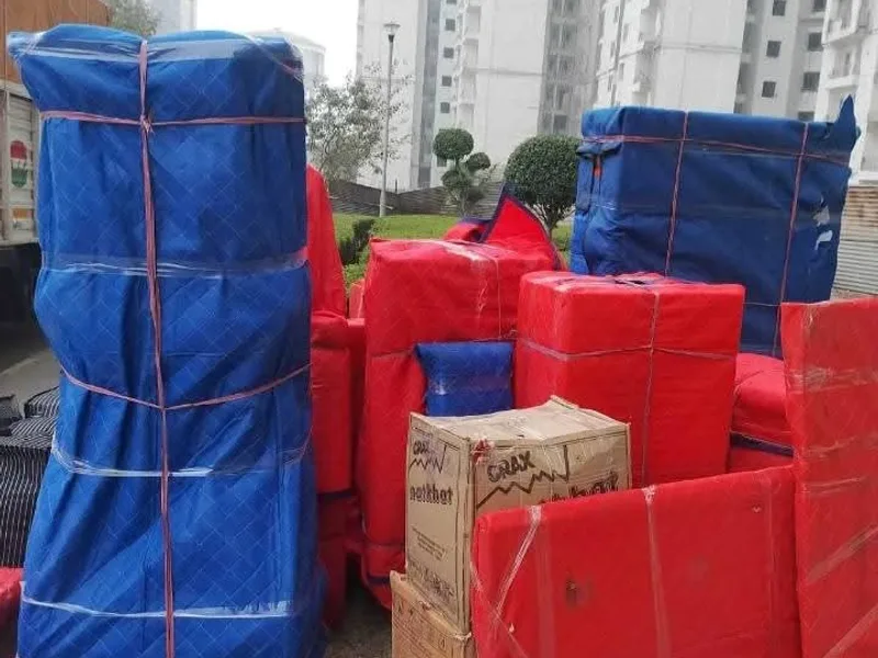 Household furniture in blue moving pads and fragile-labeled cartons staged for vehicle loading