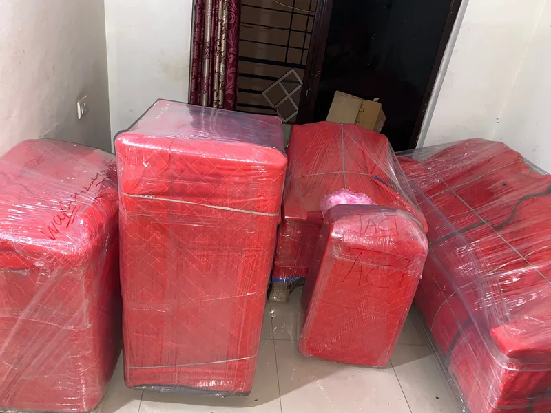 Multiple furniture pieces wrapped in protective red stretch film arranged together indoors