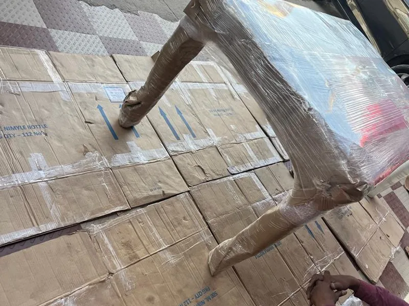 Mover wrapping wooden dining table with protective stretch wrap in driveway
